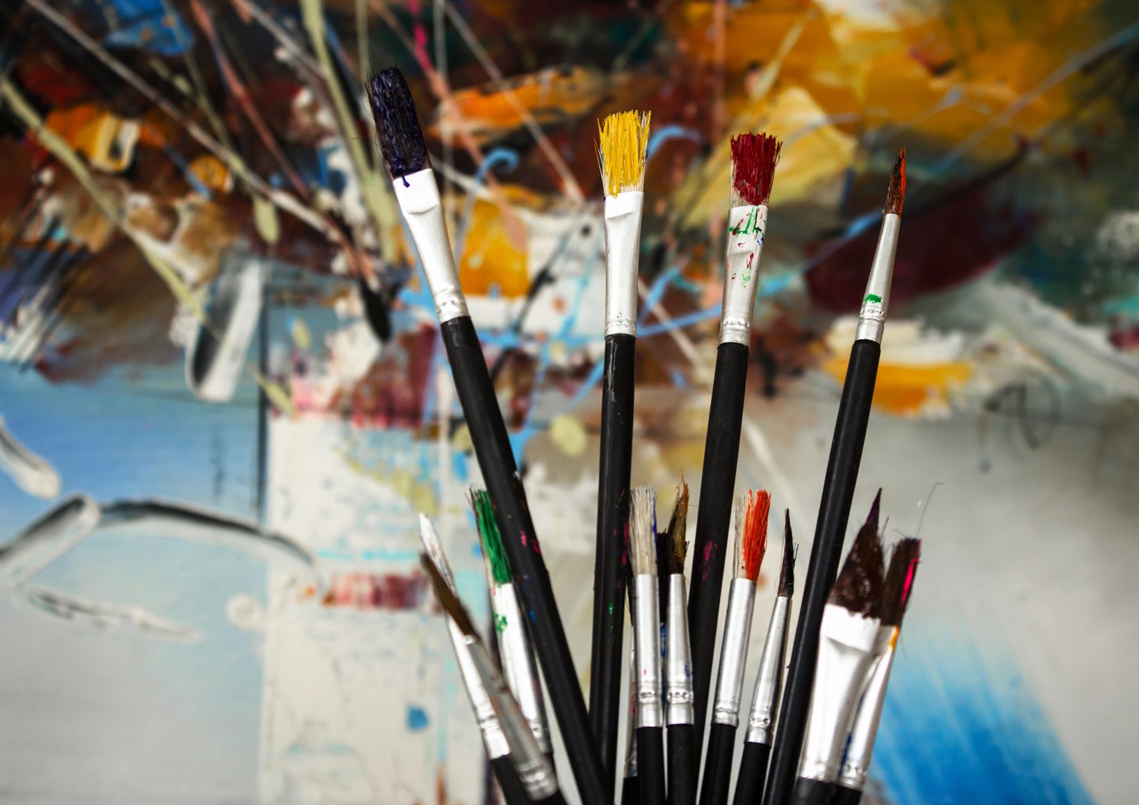 A group of paint brushes in front of a painting.