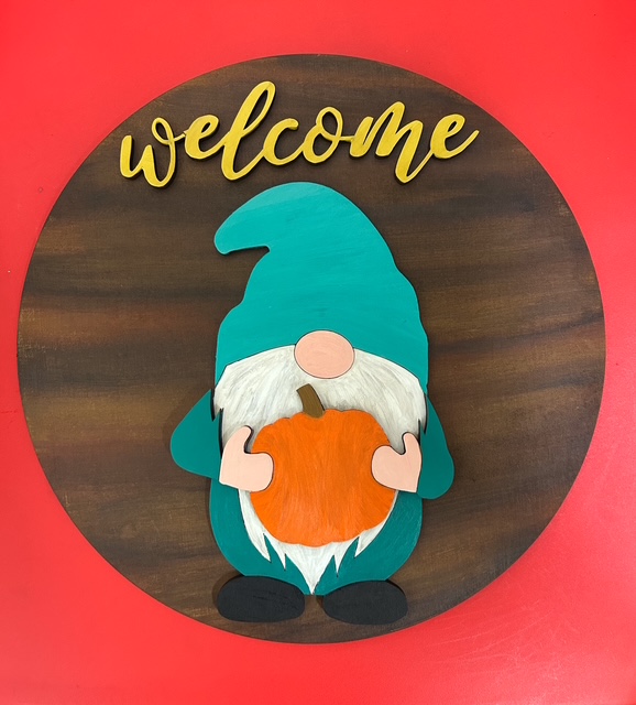 Wooden gnome holding pumpkin with welcome sign.