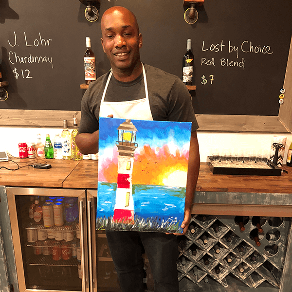A man holding a painting of a lighthouse created with paint.