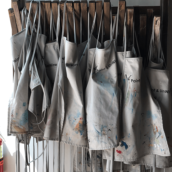 A group of aprons hanging on a paint rack.